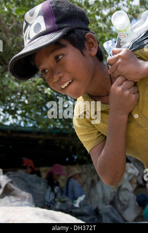 A child laborer boy is carrying a heavy sack filled with recyclable material near a large garbage dump in Phnom Penh, Cambodia. Stock Photo