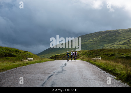 Three cyclists ride a wet path in the Scottish Highlands, Scotland, United Kingdom Stock Photo
