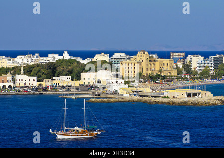 Harbour entrance of Rhodes in front of the casino and other buildings, with a sailing ship in the foreground, Rhodes Stock Photo