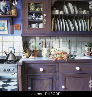 Painted purple wall cupboard with integral plate rack above matching fitted kitchen unit beside oven with Alessi kettle Stock Photo