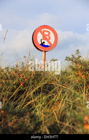 Swimming prohibited sign. Focused on the sign, surrounded by grass and sand dunes. Stock Photo