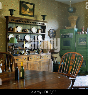 Antique mahogany table and stick back Windsor chairs in country kitchen with antique dresser and patterned wallpaper Stock Photo
