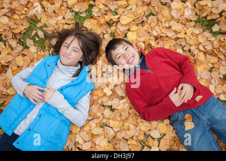 A brother and sister lay down on the ground on top of fallen leaves. Stock Photo
