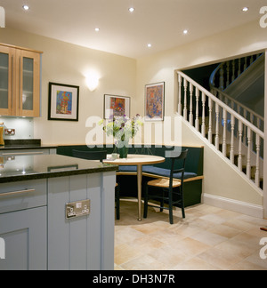 Corner banquette seating at table in modern kitchen with pale blue unit and staircase to the upper floor Stock Photo