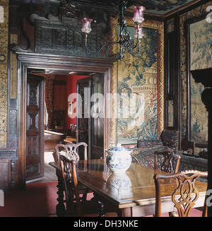 Antique medieval-style tapestry and carved wooden pediment above double doors in large dining room with Chippendale chairs Stock Photo
