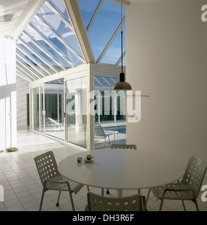 White round table and metal OMK stacking chairs in minimalist open plan dining area in large modern house with glass extension Stock Photo