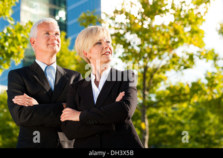 Business people - mature or senior - standing in a park outdoors in front of a office building Stock Photo