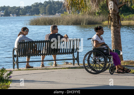 Woman sitting in wheelchair accompanied by couple in waterfront public park in Mount Dora, Florida overlooking harbor. Stock Photo