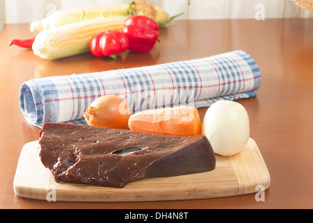 a piece of raw beef liver with vegetables on the cutting board Stock Photo