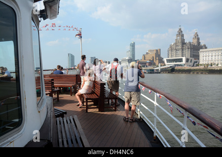 Tourists taking pictures of The Royal Liver building seen through flags from a Mersey ferry arriving at the Pier Head. Stock Photo