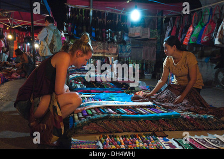Horizontal close up of a Caucasian tourist looking at textiles at a Laos street market at night.