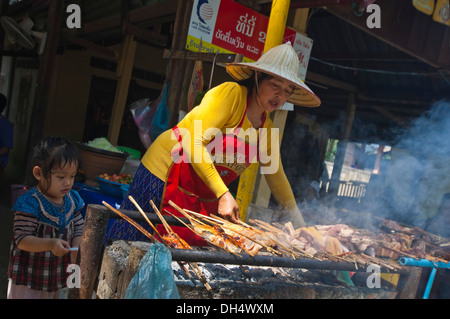 Horizontal portrait of a local Lao lady and her daughter grilling kebabs on a BBQ at a roadside restaurant. Stock Photo