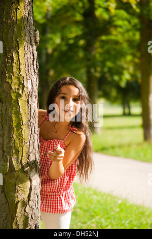 Smiling girl looking out from behind a tree Stock Photo