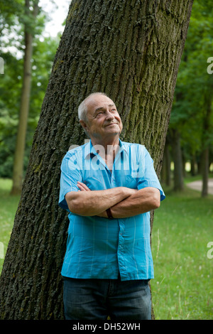 Elderly man leaning against a tree, in a good mood Stock Photo