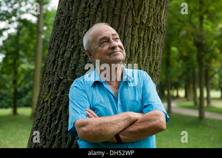 Elderly man leaning against a tree, in a good mood Stock Photo