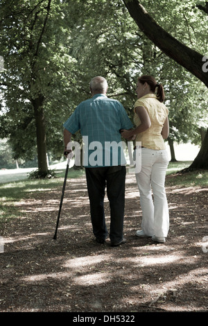 A woman and an elderly man with a walking cane taking a walk in the park Stock Photo