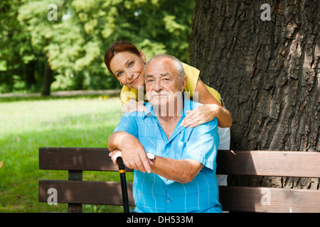 Women looking after an elderly man sitting on a bench in a park Stock Photo