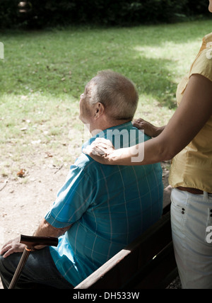 Women looking after an elderly man sitting on a bench in a park Stock Photo