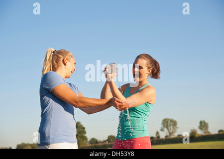 Two young women having fun with a bottle of water during a drink break while doing sports Stock Photo