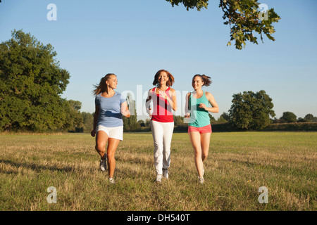 Three young women jogging together across a meadow Stock Photo