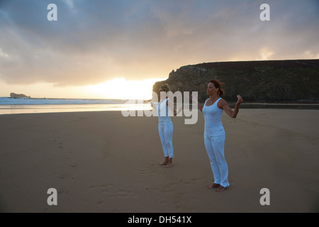 Two women relaxing by doing yoga on the beach at sunset Stock Photo