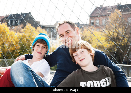 Two cool boys sitting with their father on a playground Stock Photo