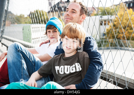 Two cool boys sitting with their father on a playground Stock Photo