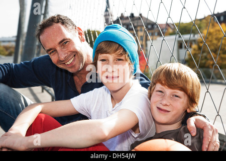 Two cool boys sitting with their father on a playground Stock Photo