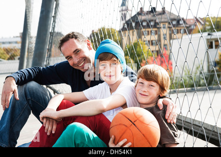 Two cool boys sitting with their father on a playground Stock Photo
