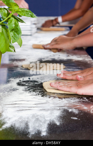 Detail of children's hands making pizza bases. Basil leaves in foreground. Stock Photo