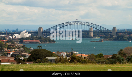 Panoramic city landscape showing Sydney harbour bridge, iconic opera house, and houses beside blue waters of Darling Harbour Stock Photo