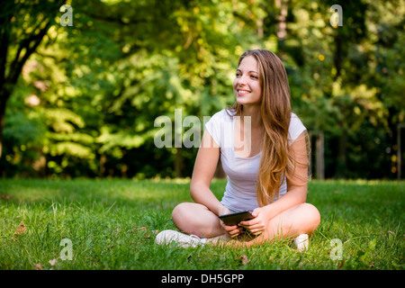 Young woman (teen girl) reading book on electronic book reader - outdoor in nature Stock Photo