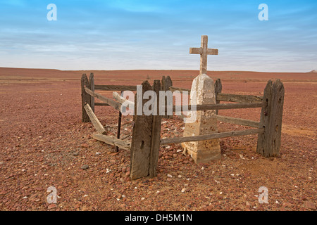 Solitary grave of pioneer on barren stone plains of arid Australian outback landscape stretching to horizon with blue sky Stock Photo