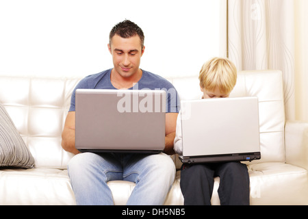 Father and son working on their computers on the sofa at home Stock Photo