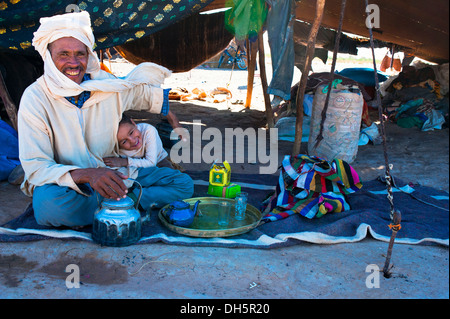 Friendly nomad, Berber, sitting with his son on the floor smiling and preparing tea in front of his nomad tent, Erg Chebbi Stock Photo