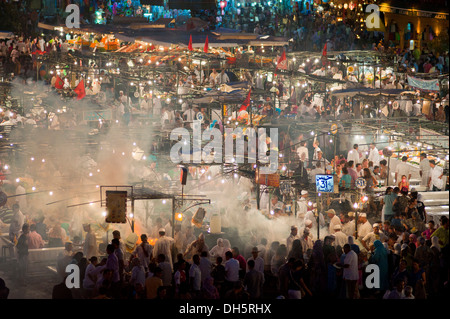 Countless people are eating at the food stalls in Jemaa el Fna square at night, white smoke rising from the cooking areas and Stock Photo