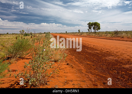 Landscape with long red dirt road of Sandover Highway slicing across plains of Australian outback landscape Northern Territory Stock Photo
