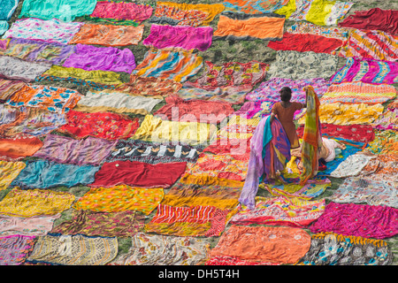 Colourful saris are laid out on the sand for drying after washing, an Indian woman is collecting the dried saris, Agra Stock Photo