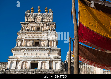 Depiction of gods and figures in white marble on a shikhara tower of a Hindu temple, next to an awning made of coloured fabrics Stock Photo