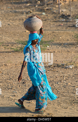 Indian woman wearing a light blue sari carrying a clay water jug on her head, Khuri, Rajasthan, India Stock Photo
