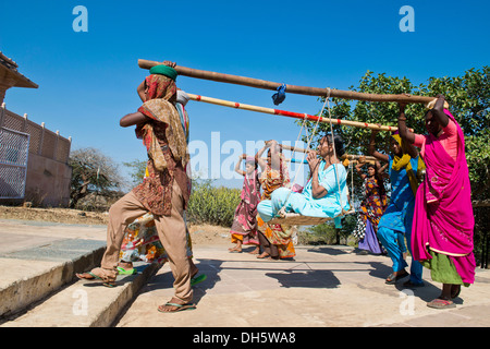 Young Indian women wearing traditional saris carrying long bamboo poles on their heads with a seat for pilgrims climbing the Stock Photo