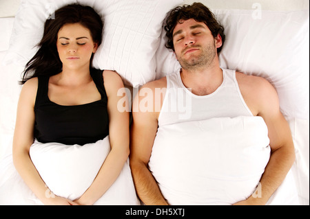 Beautiful couple laid in a white bed sleeping next to each other Stock Photo