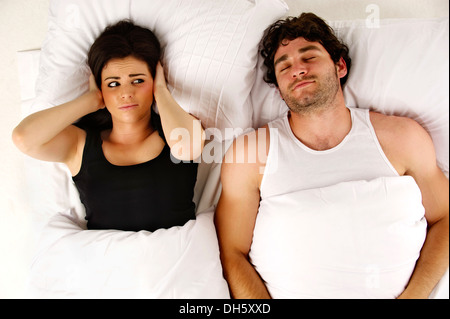 Beautiful woman laid in a white bed awake next to her sleeping snoring boyfriend isolated on a white background Stock Photo