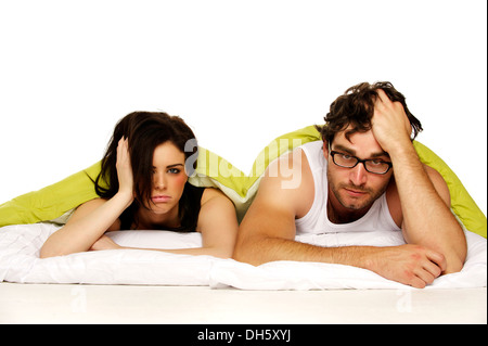 Attractive couple laid in bed under a green duvet looking tired and miserable in the morning Stock Photo