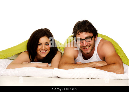 Attractive couple laid in bed under a green duvet smiling at the camera Stock Photo