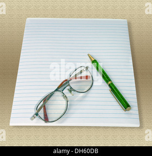 Writing pad with reading glasses and bright green ballpoint pen on light coloured fabric background Stock Photo
