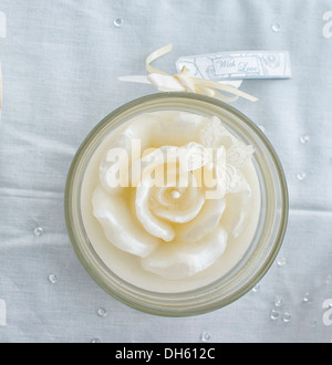 Rose shaped wedding candle in glass jar on tablecloth, attached is a  with love label Stock Photo