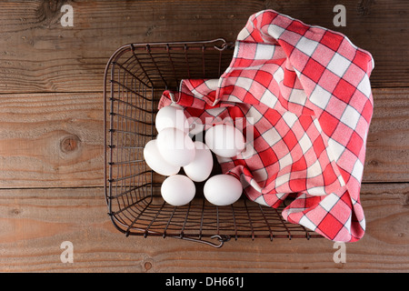 A wire basket with eggs and a red checkered napkin on a rustic wood surface. Stock Photo