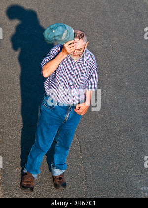 Overhead rear view of elderly man walking across road / raising hat / scratching head - France. Stock Photo