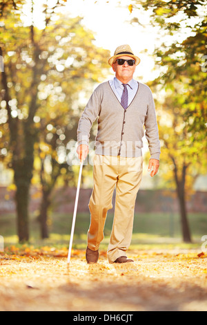 Blind mature person holding a stick and walking in a park Stock Photo